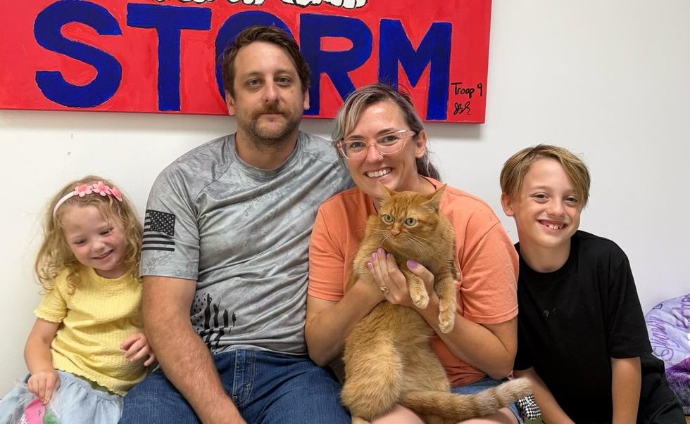 A family sits together beneath an Orphans of the Storm banner, the mother holding their new orange cat.