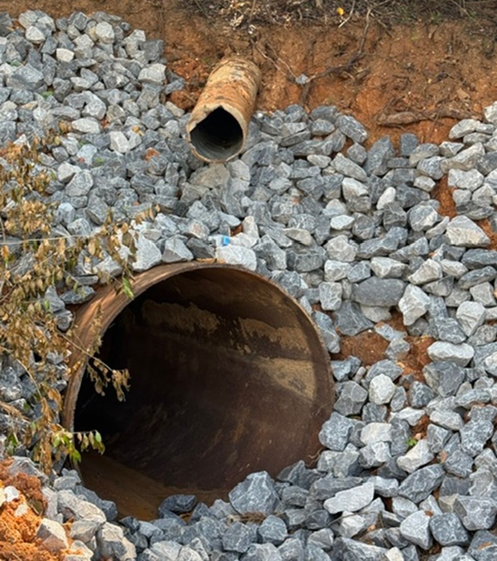 A large drain pipe set into a rocky embankment beside a dirt hillside.